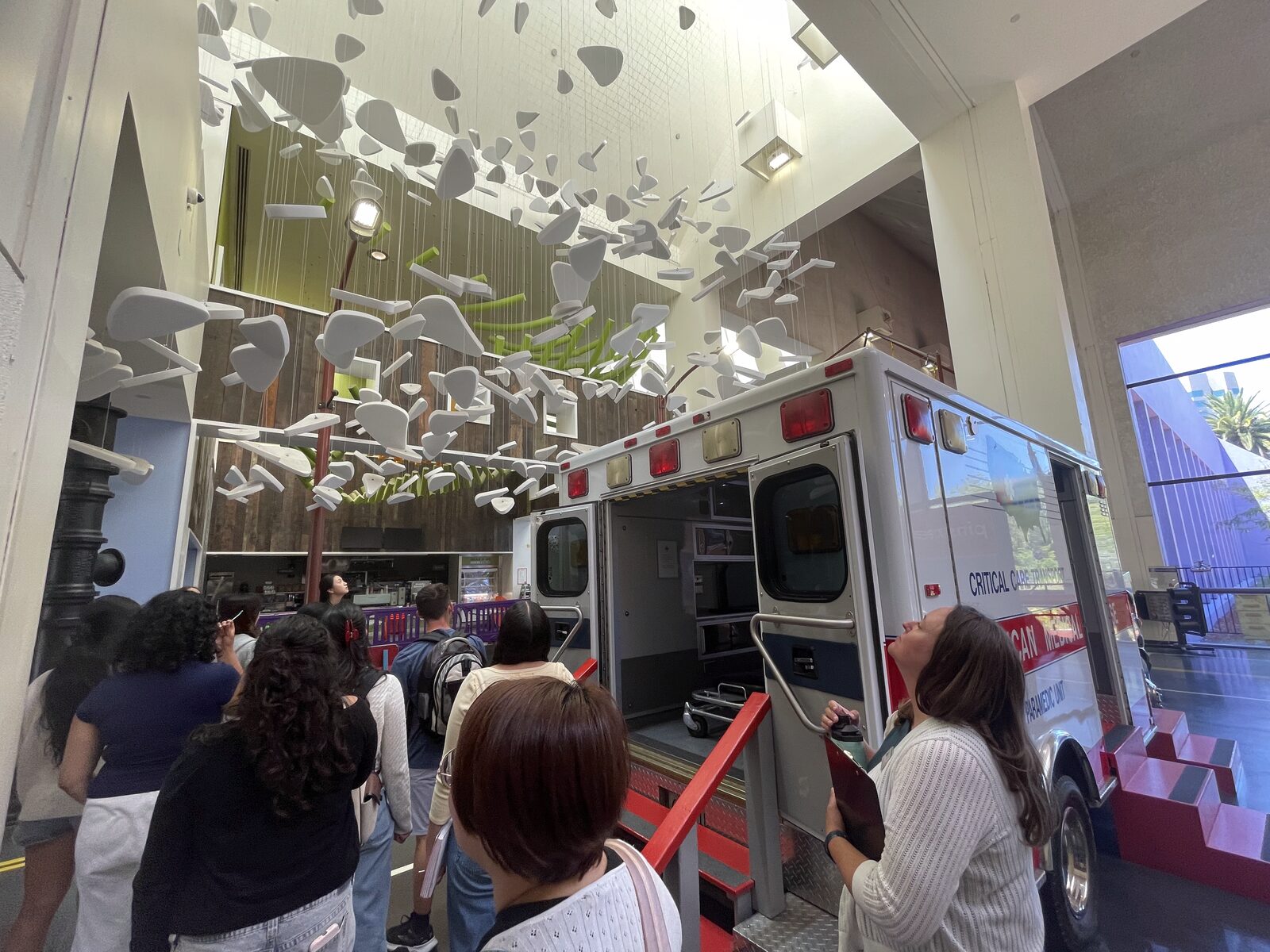 Students looking at a real ambulance exhibit beneath a hanging paper installation