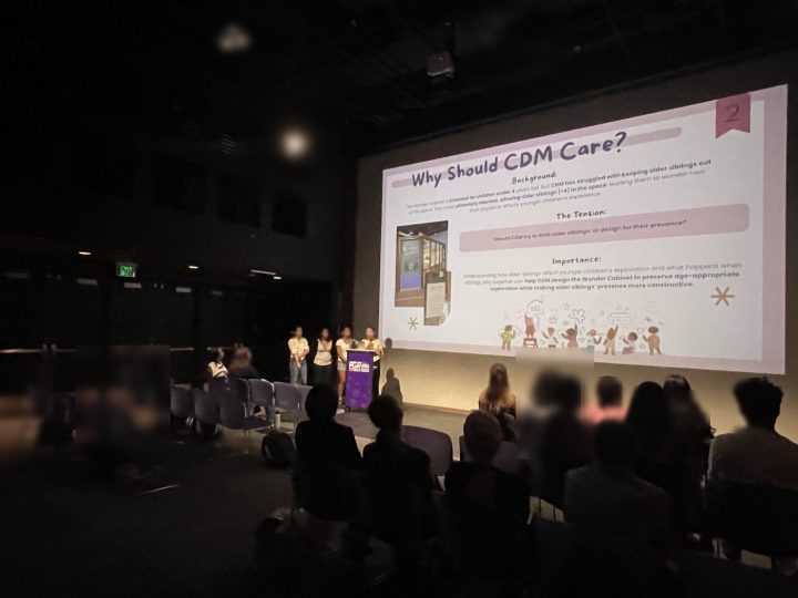 A student team presenting to a seated audience in the museum theater
